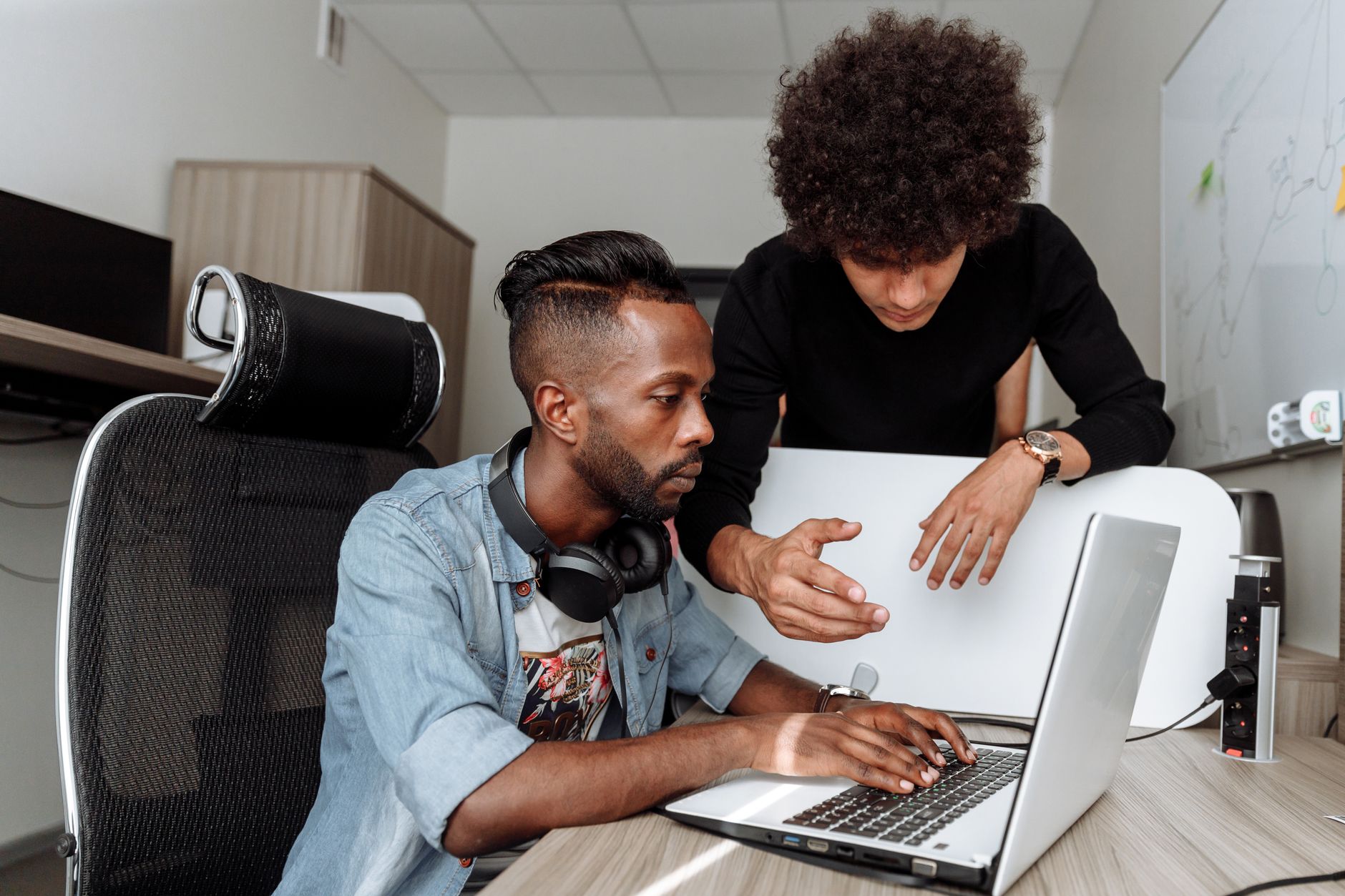 Two diverse male colleagues collaborating on a laptop in a modern office environment.