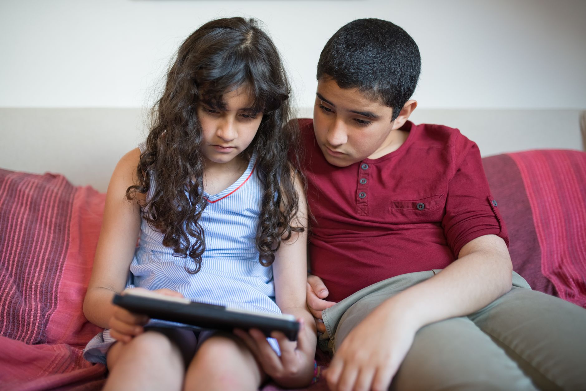 Two children sitting indoors in Portugal, focused on a tablet, showcasing modern technology use.