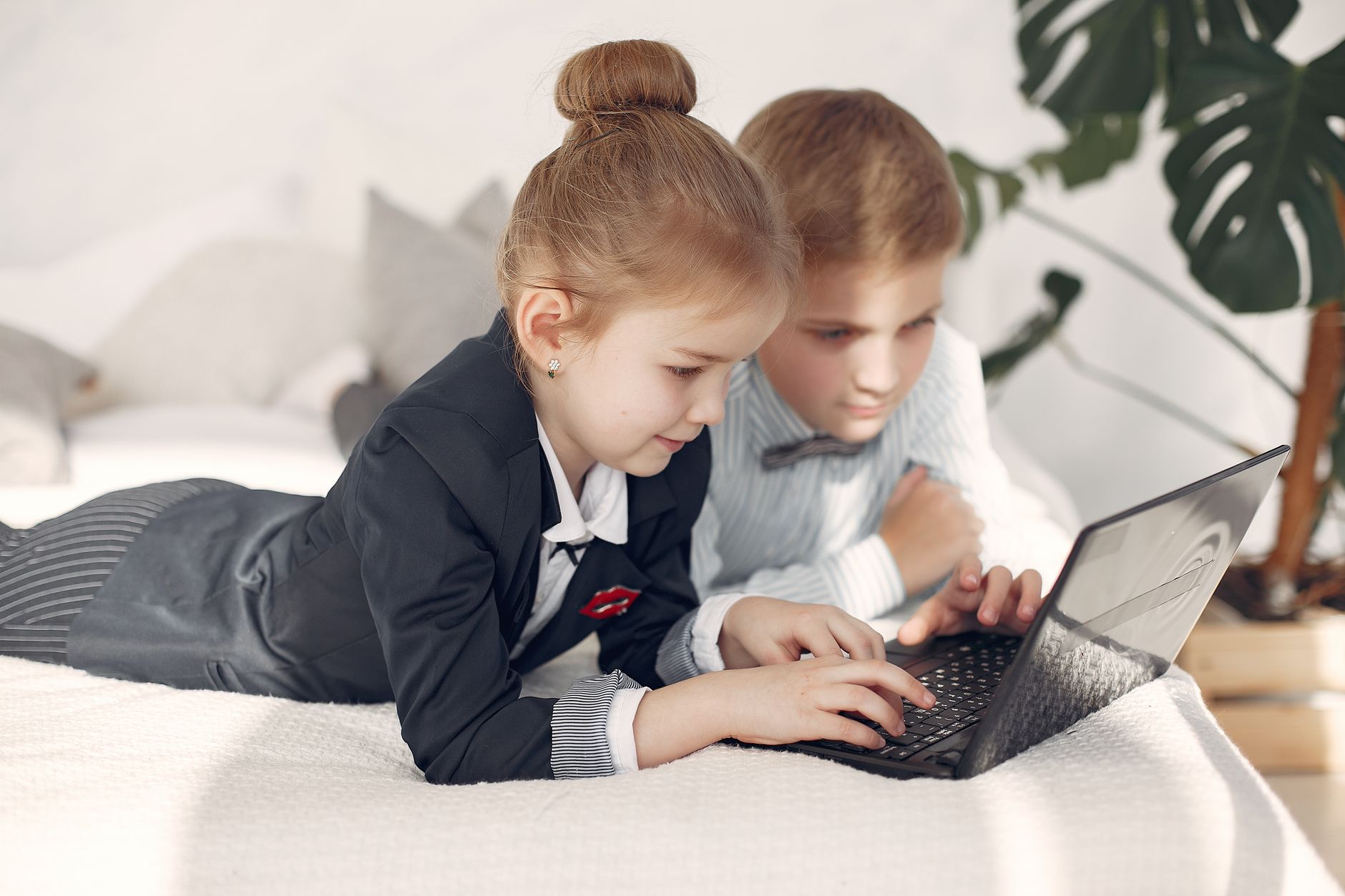 Positive cute boy and girl wearing formal clothing lying on bed together and browsing netbook during teamwork at home