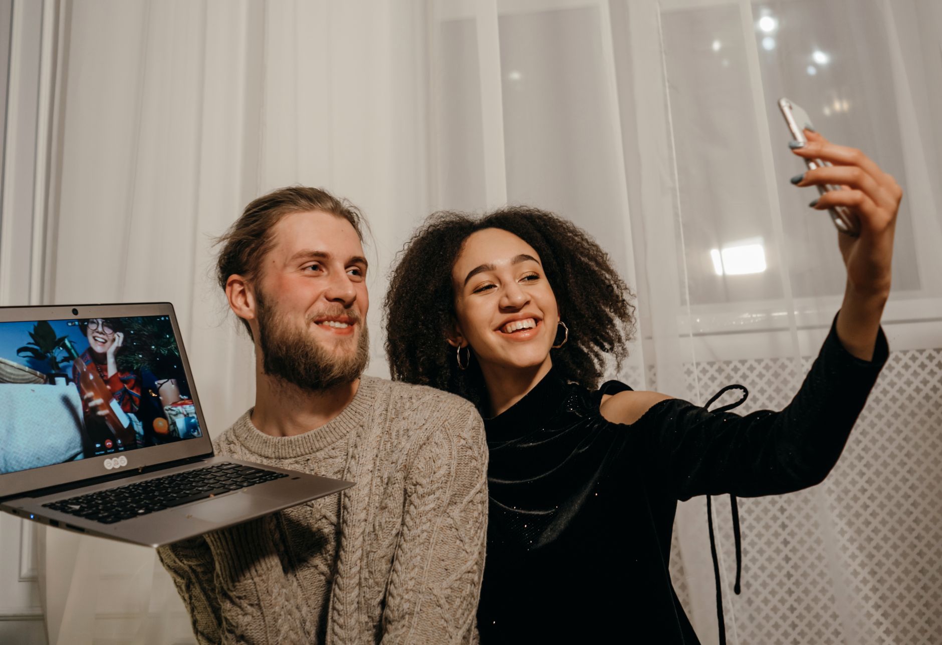 Couple smiling and taking a selfie during a festive video call at home.
