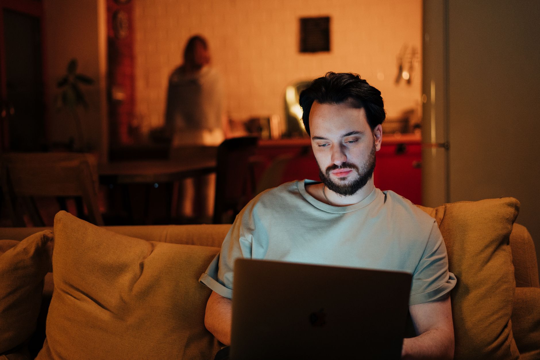 Man working on laptop at home, cozy evening atmosphere with warm light.