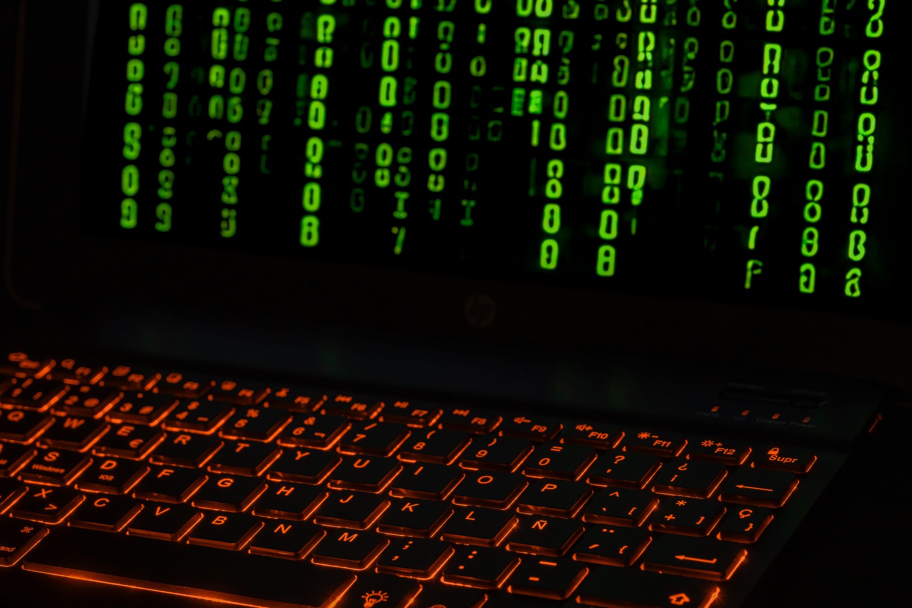 A laptop keyboard with orange backlight displaying green digital code symbols.