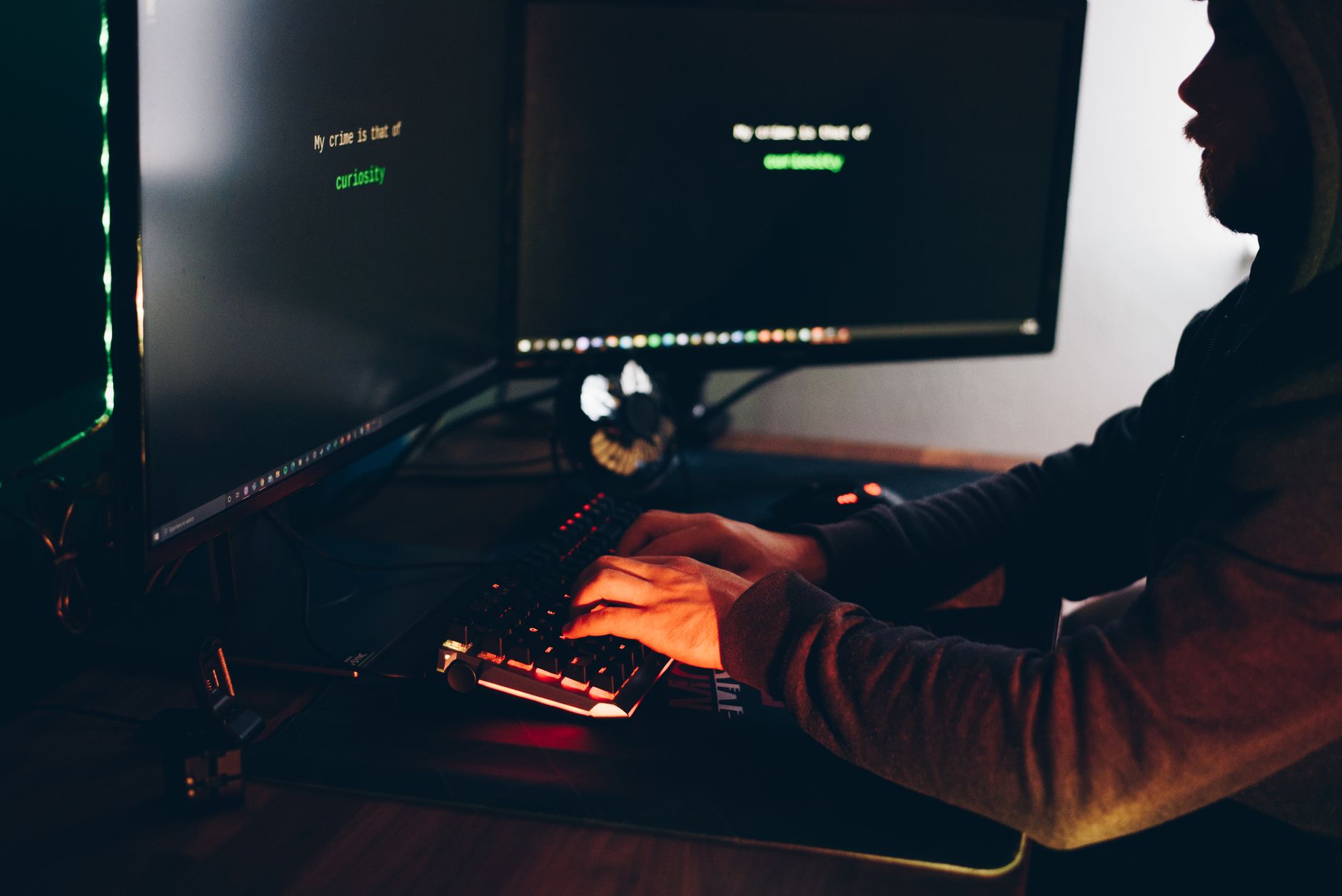 Side view of crop anonymous male cyber thief accessing information on desktop computer screens at dusk