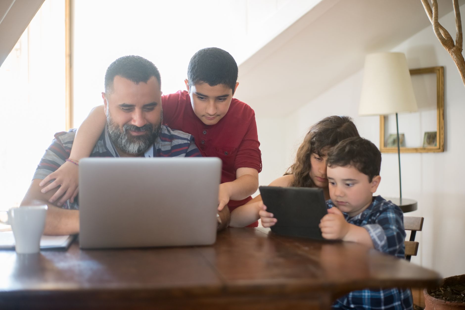 Father and kids engaging with a laptop and tablet in a cozy home setting.