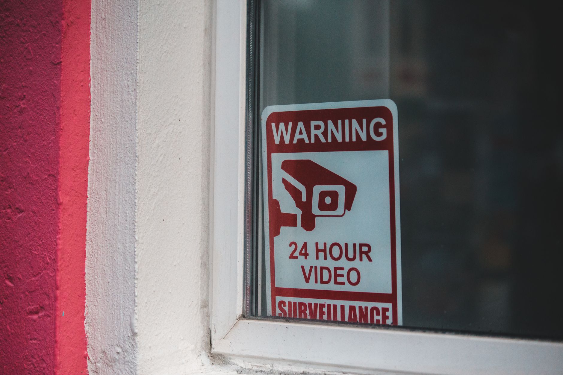 Red warning sign of video surveillance placed behind window of building in daytime