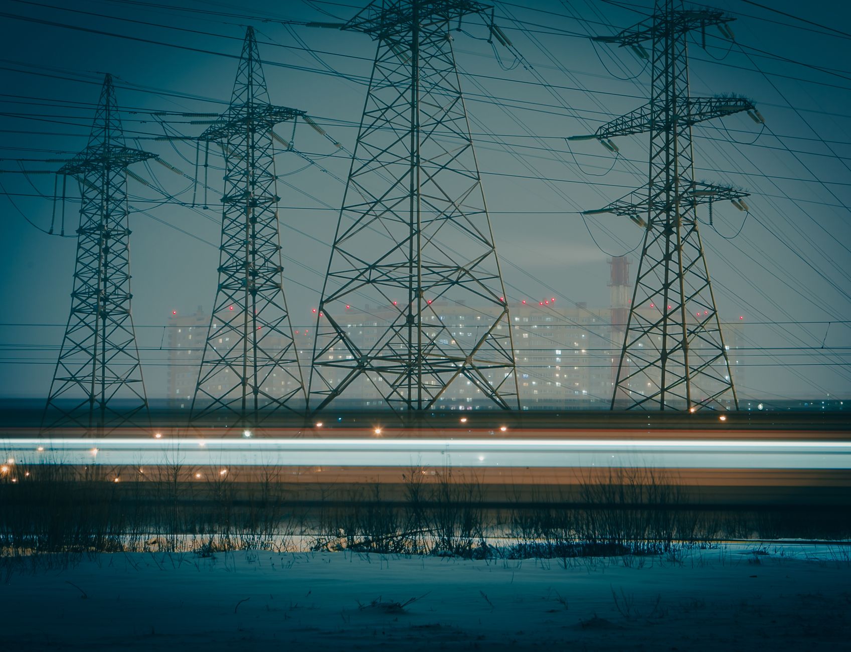 Moody night photo of electric towers silhouetted against an urban cityscape, highlighting powerful infrastructure.