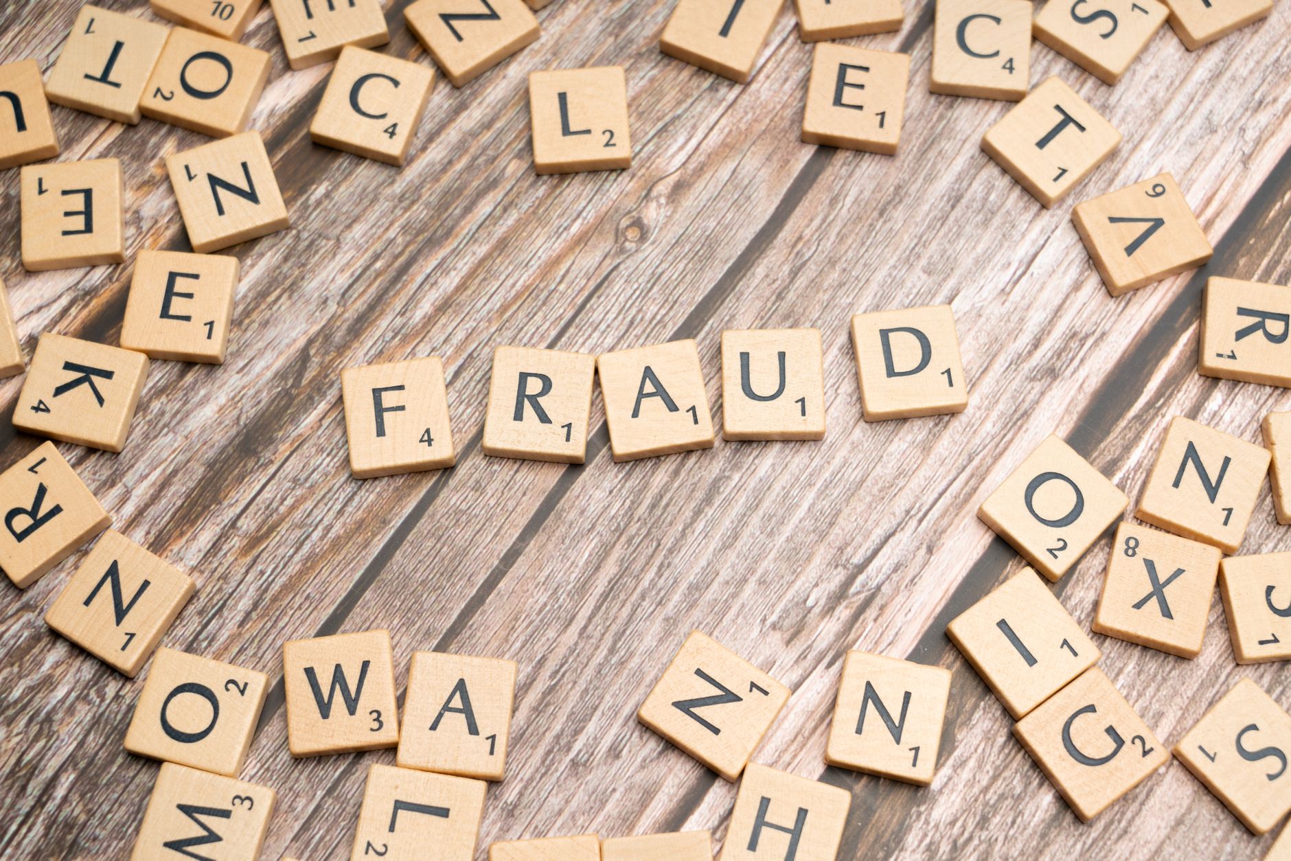 Alphabet tiles arranged to spell 'fraud' on a wooden surface, symbolizing deception.