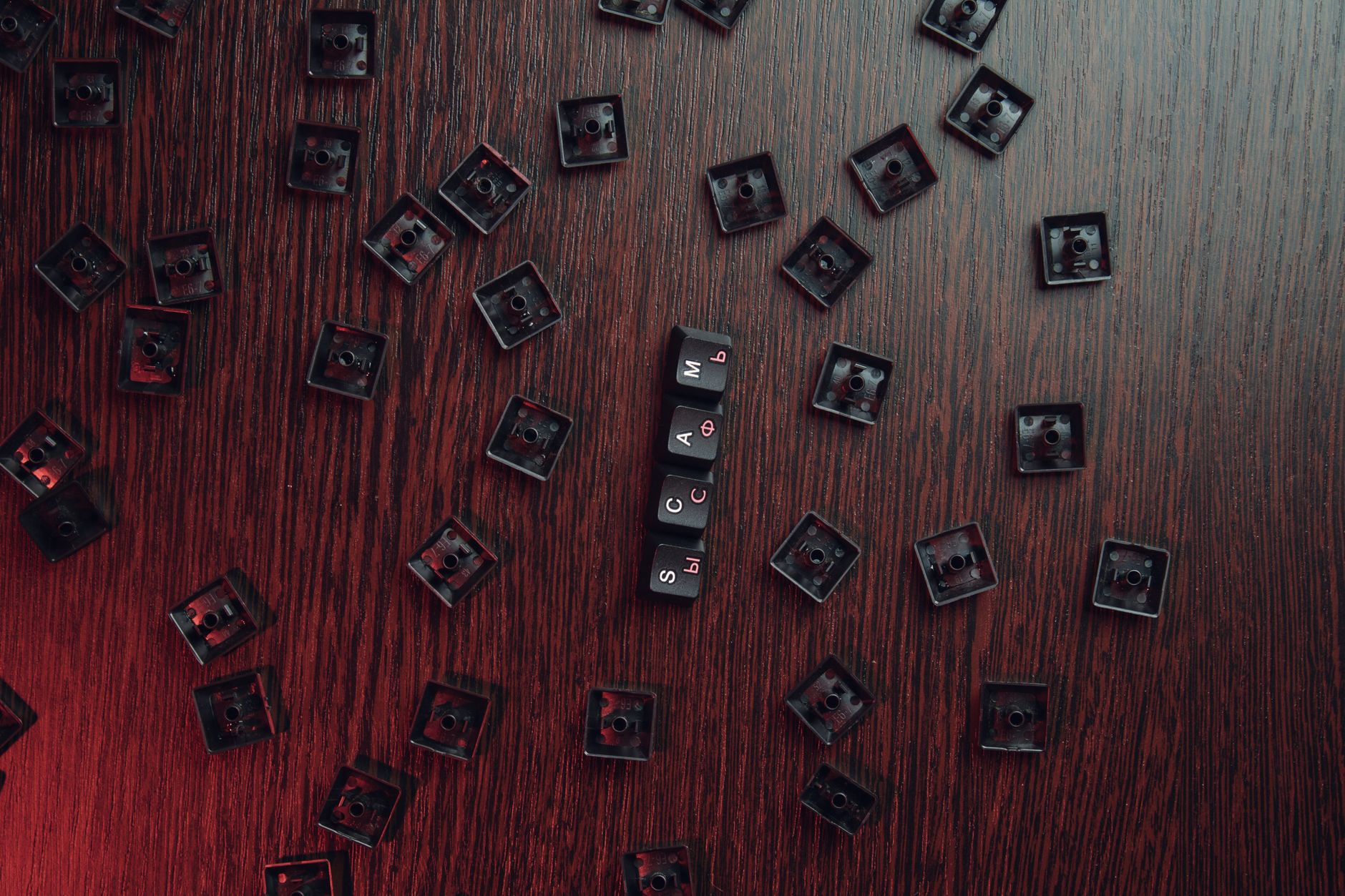 Aerial view of scattered keyboard keycaps on a wooden surface with 'SCAM' spelled out.
