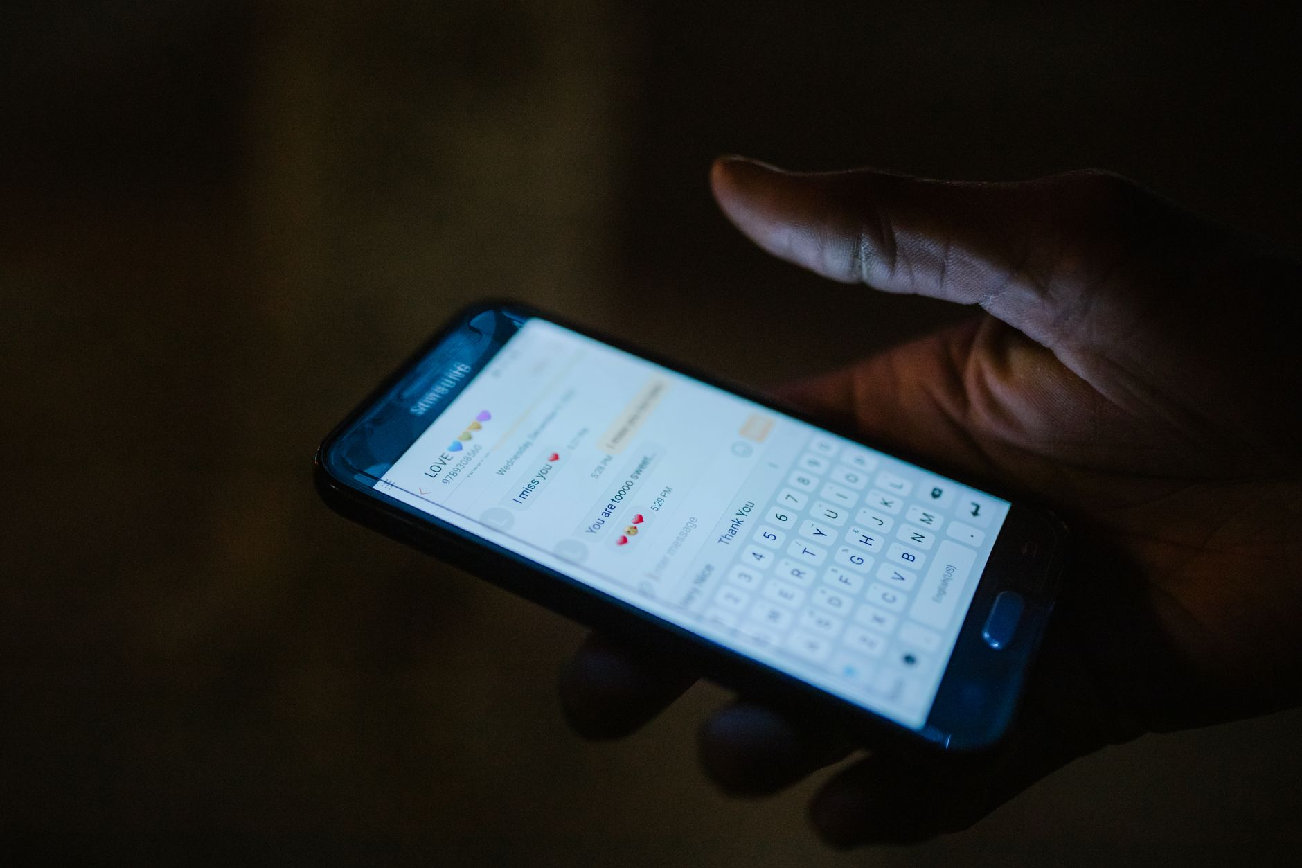 Close-up of a hand holding a smartphone with a messaging app open, illuminated by screen light.