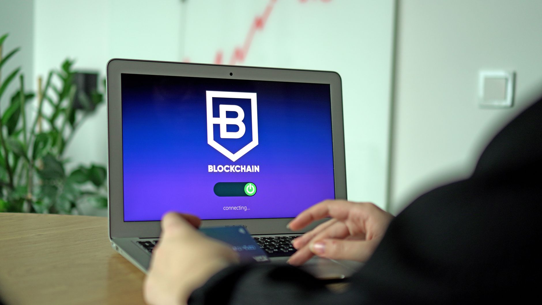 Hand holding a card near a laptop displaying blockchain connection screen.