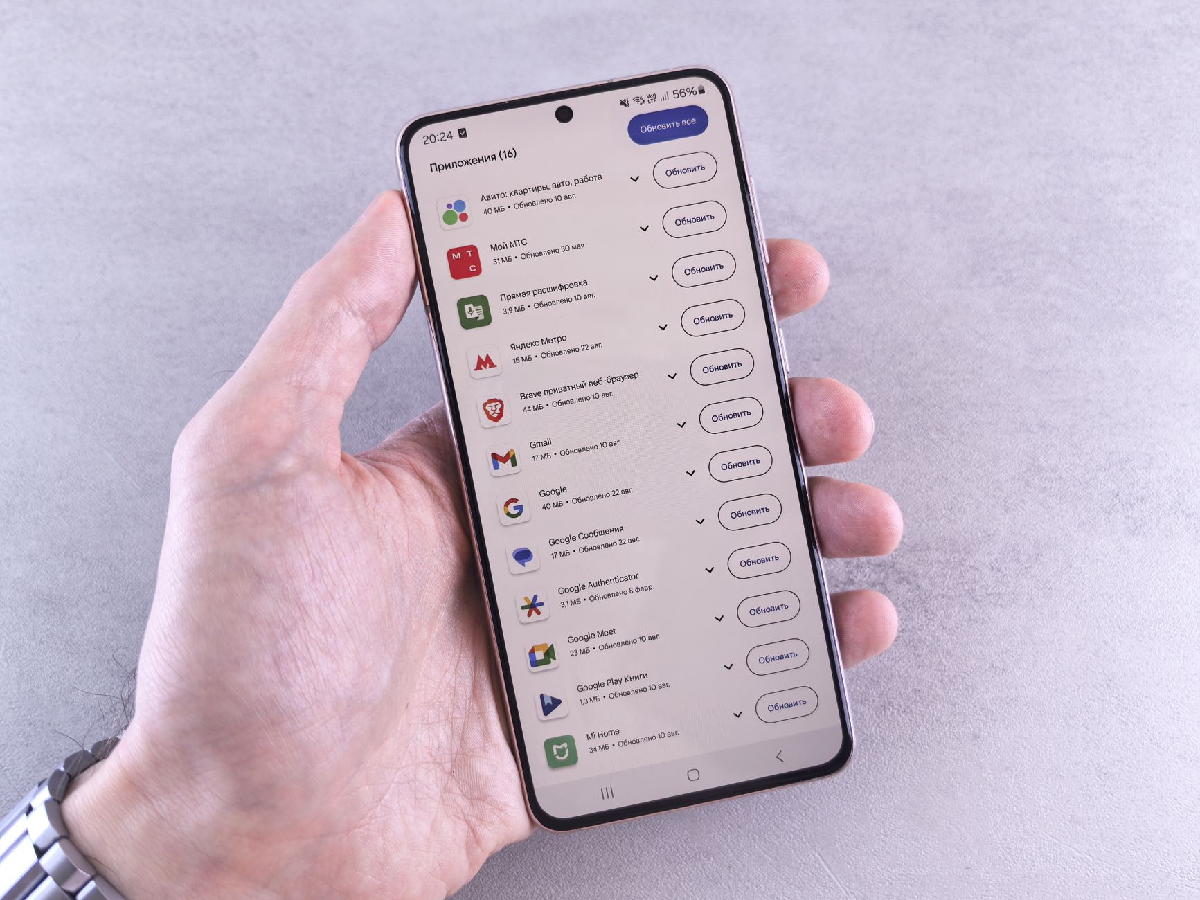 Close-up of a hand holding a smartphone displaying app updates on a light background.
