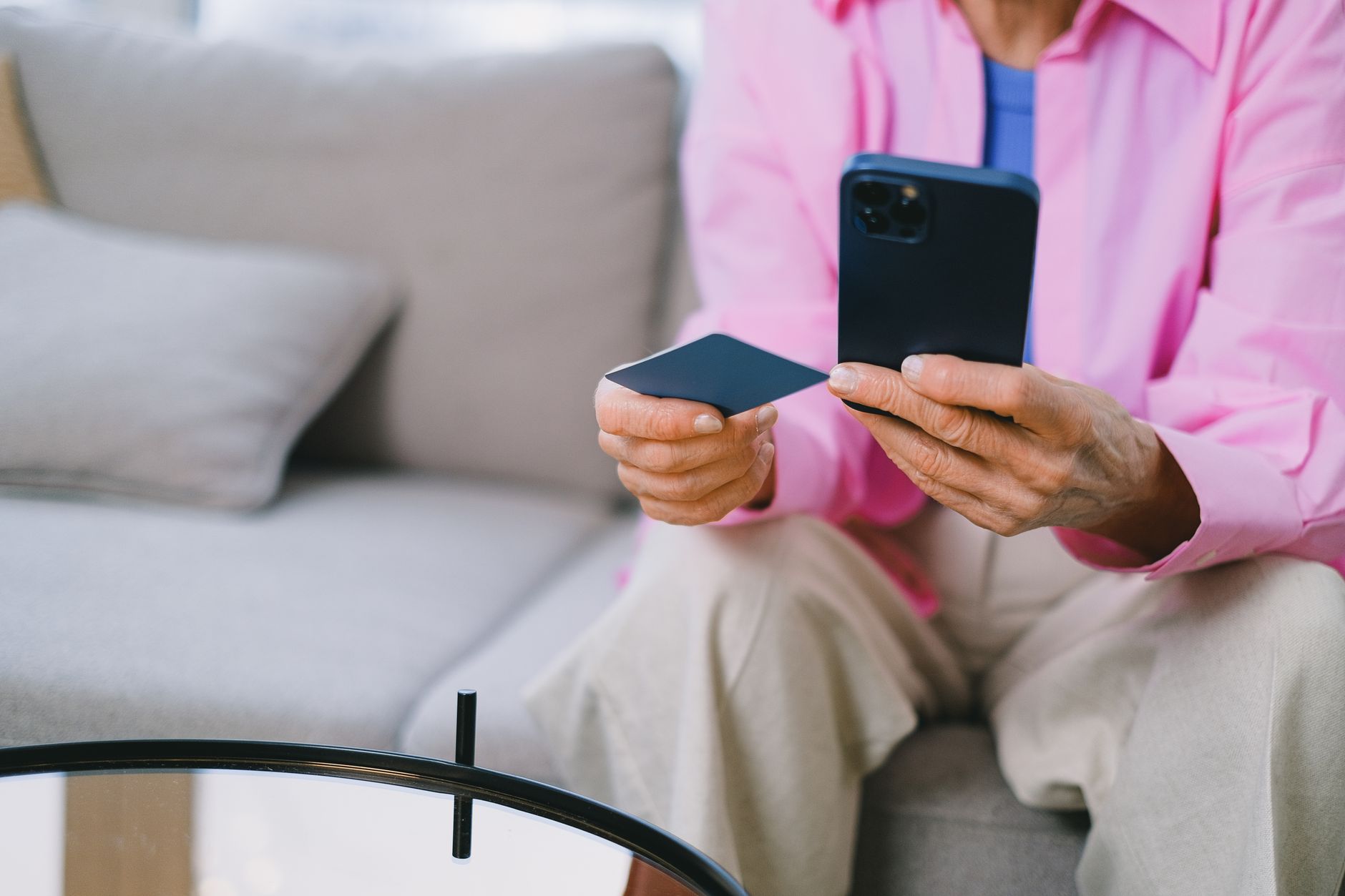 Elderly person making an online payment with credit card using smartphone, seated indoors.