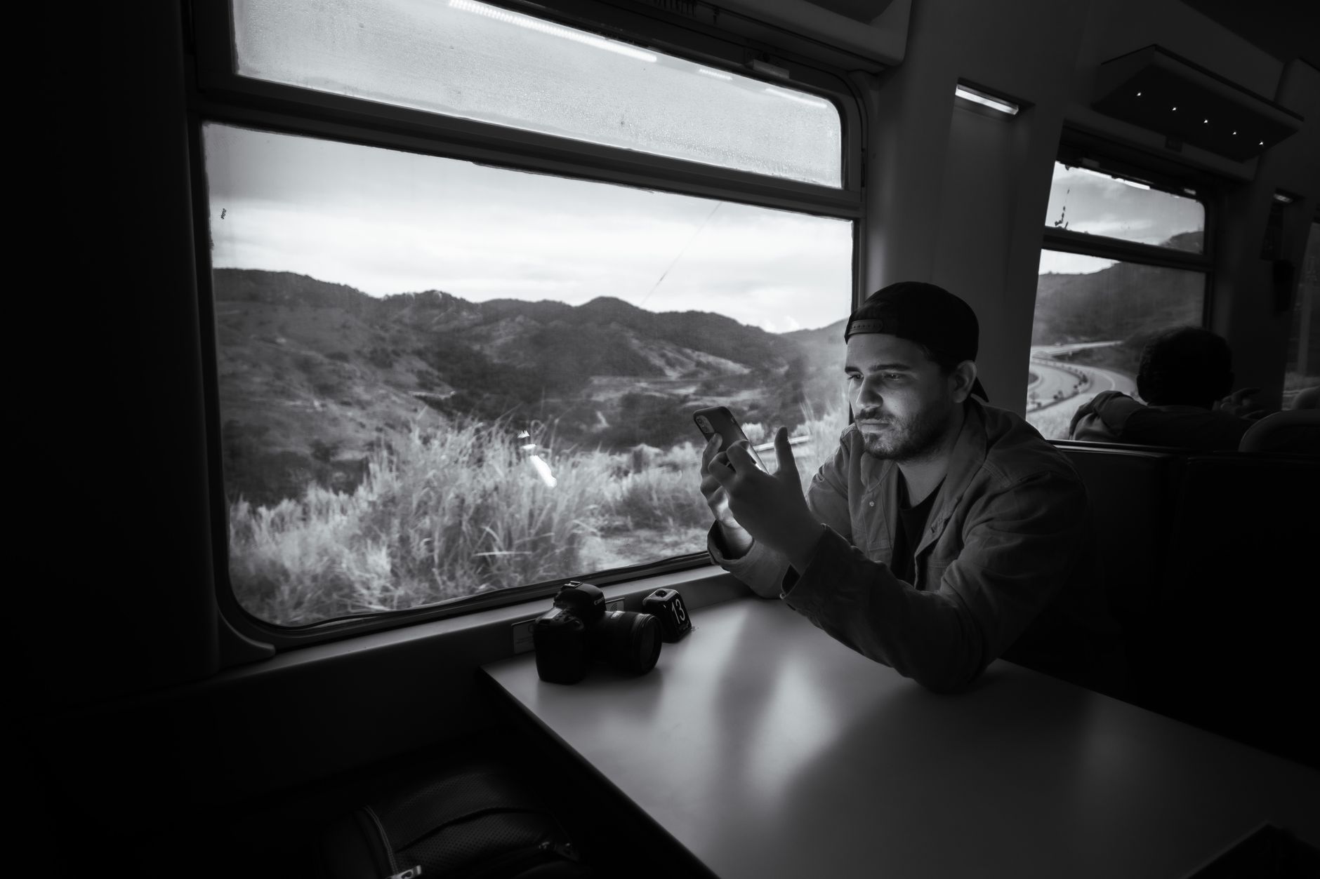 Man using a smartphone on a train journey through scenic landscape.